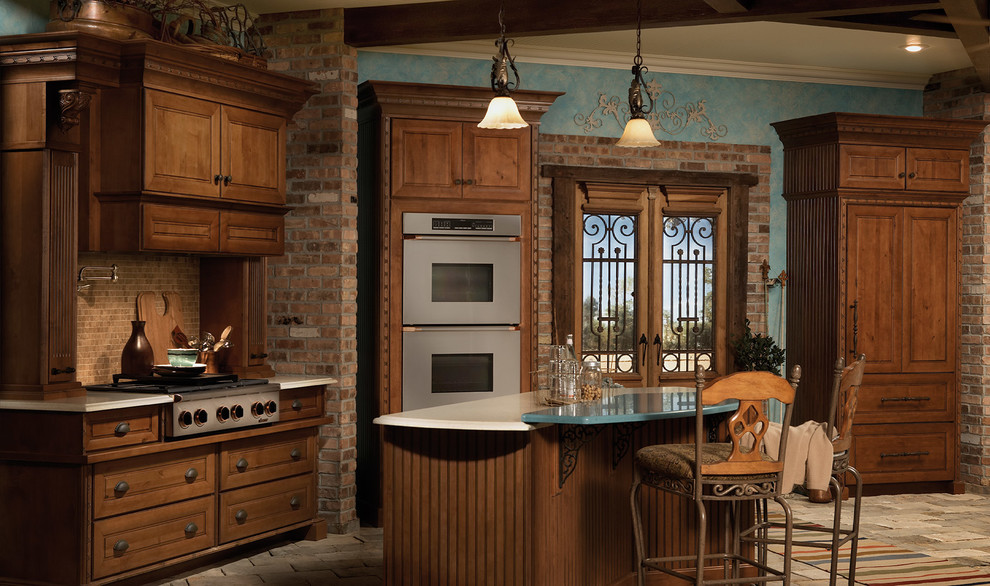 Bild på ett medelhavsstil kök, med luckor med infälld panel, skåp i mellenmörkt trä, brunt stänkskydd, stänkskydd i stenkakel, rostfria vitvaror, tegelgolv och en köksö