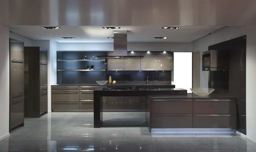 Diseño de cocina actual con armarios con paneles lisos, puertas de armario grises, salpicadero negro, salpicadero de vidrio templado y electrodomésticos con paneles