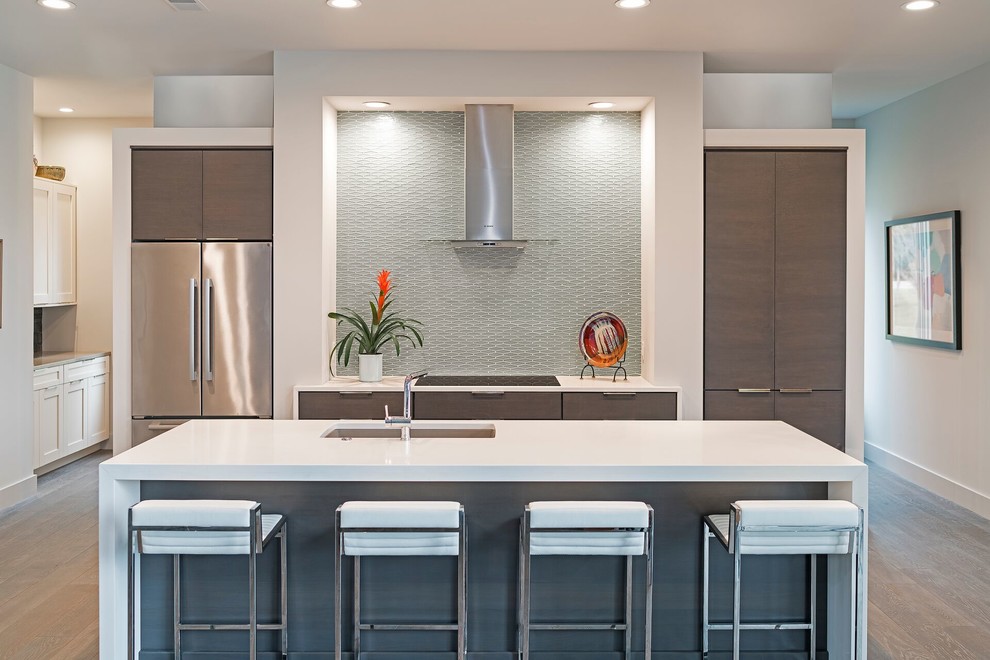 Moderne Küche mit Unterbauwaschbecken, flächenbündigen Schrankfronten, braunen Schränken, Küchenrückwand in Grau, Rückwand aus Glasfliesen, Küchengeräten aus Edelstahl, Kücheninsel und dunklem Holzboden in Charleston