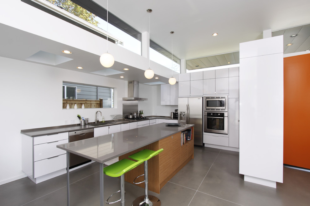 Mid-sized minimalist l-shaped concrete floor enclosed kitchen photo in Seattle with stainless steel appliances, an undermount sink, flat-panel cabinets, white cabinets, solid surface countertops and an island