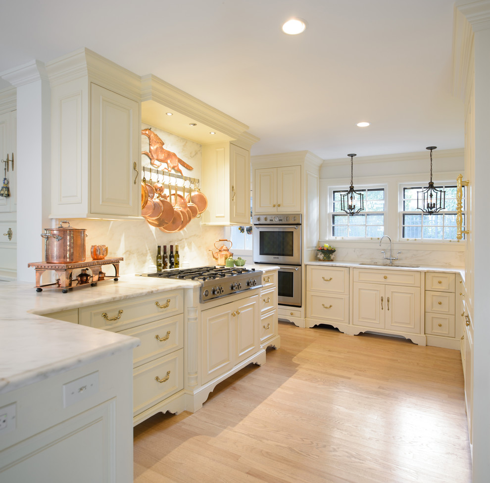 Inspiration for a medium sized classic u-shaped kitchen/diner in Kansas City with white cabinets, white splashback, stone slab splashback, a double-bowl sink, raised-panel cabinets, marble worktops, stainless steel appliances and light hardwood flooring.