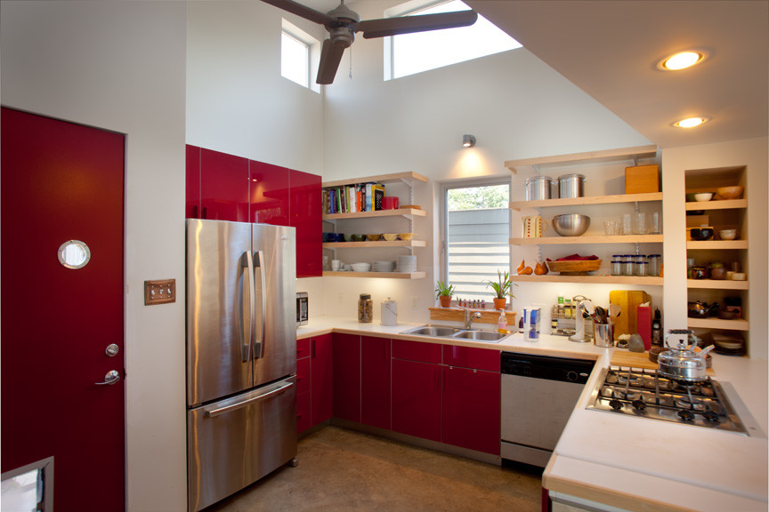 Modern inredning av ett mellanstort kök, med en nedsänkt diskho, släta luckor, röda skåp, träbänkskiva, vitt stänkskydd, stänkskydd i keramik, rostfria vitvaror och betonggolv