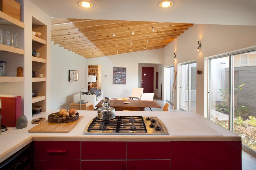 Example of a mid-sized trendy u-shaped concrete floor eat-in kitchen design in Houston with a drop-in sink, flat-panel cabinets, red cabinets, wood countertops, white backsplash, ceramic backsplash, stainless steel appliances and no island