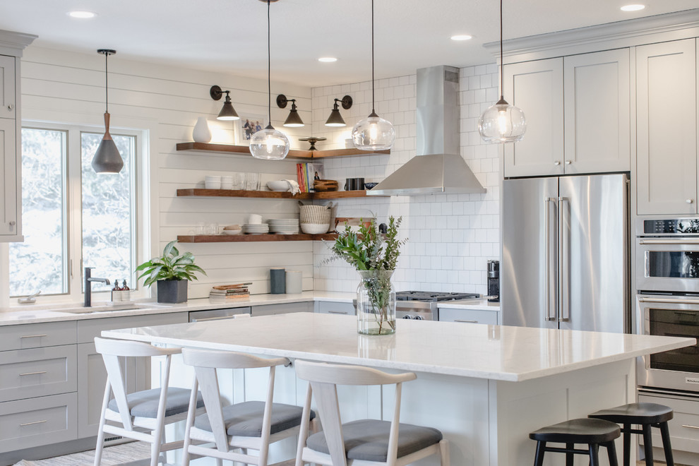 Inspiration pour une cuisine traditionnelle en L avec un évier encastré, un placard à porte shaker, des portes de placard grises, une crédence blanche, un électroménager en acier inoxydable, îlot et un plan de travail blanc.