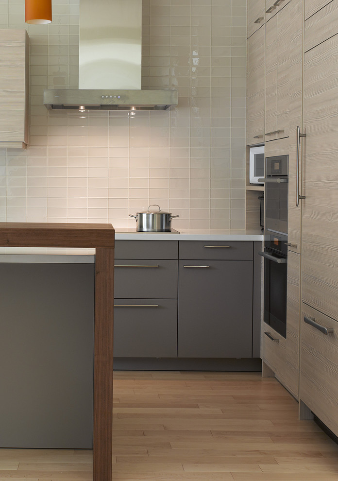 Diseño de cocina moderna con armarios con paneles lisos, puertas de armario grises, salpicadero de azulejos de vidrio, electrodomésticos con paneles y salpicadero blanco