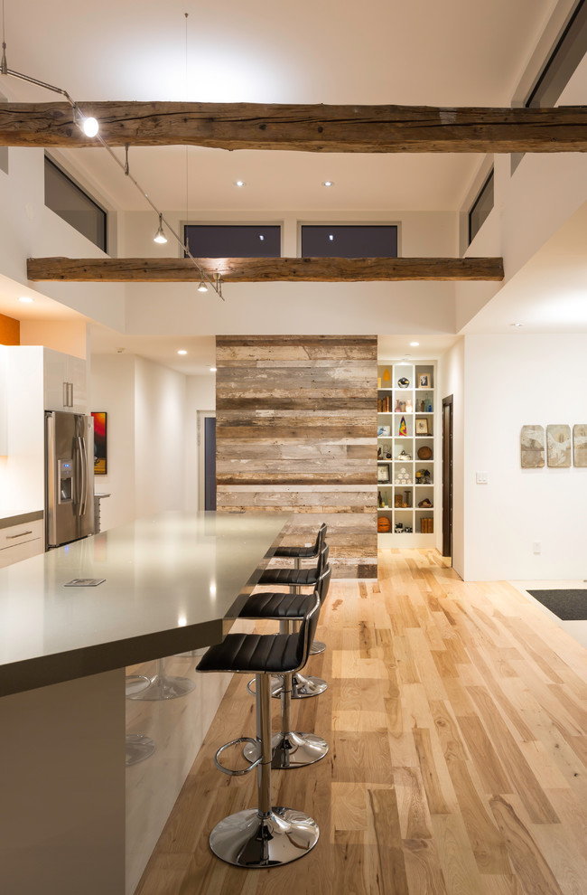 Imagen de cocina contemporánea abierta con encimera de acrílico, electrodomésticos de acero inoxidable, suelo de madera clara y una isla