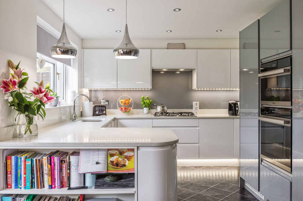 Inspiration for a medium sized contemporary u-shaped kitchen in Other with a submerged sink, flat-panel cabinets, white cabinets, grey splashback, stainless steel appliances, grey worktops, a breakfast bar and grey floors.