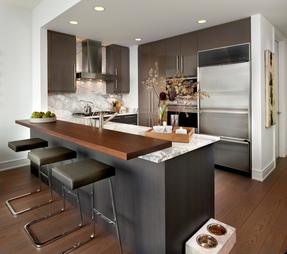 Photo of a contemporary u-shaped kitchen/diner in Chicago with flat-panel cabinets, white splashback, stainless steel appliances, dark hardwood flooring, a submerged sink, stone slab splashback and brown cabinets.