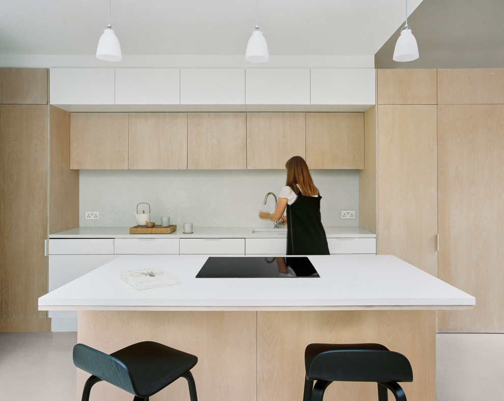 Example of a mid-sized minimalist single-wall concrete floor, pink floor and tray ceiling open concept kitchen design in London with a drop-in sink, flat-panel cabinets, light wood cabinets, quartz countertops, gray backsplash, quartz backsplash, black appliances, an island and white countertops