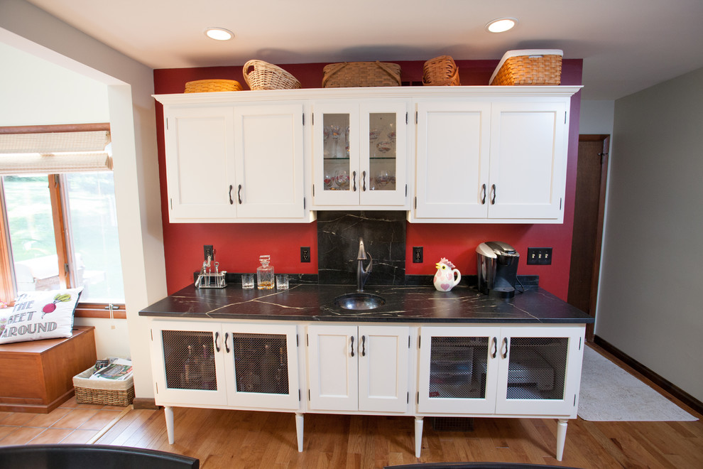 Lantlig inredning av ett mellanstort kök, med en rustik diskho, luckor med upphöjd panel, skåp i mellenmörkt trä, granitbänkskiva, beige stänkskydd, stänkskydd i stenkakel, rostfria vitvaror, ljust trägolv och en halv köksö