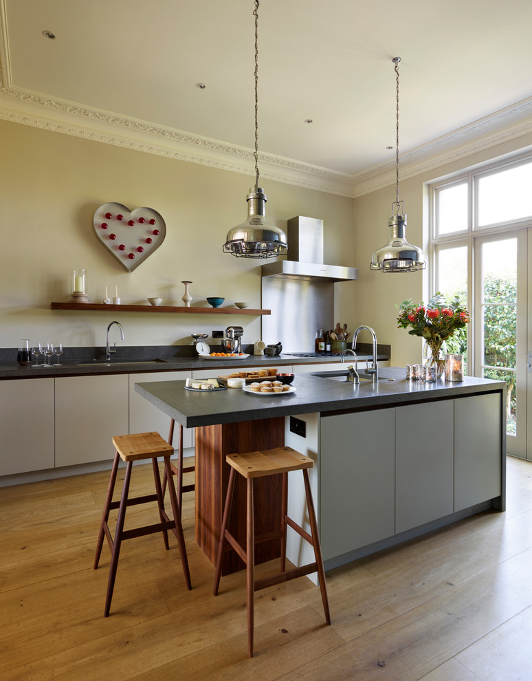 Example of a large trendy single-wall light wood floor and brown floor open concept kitchen design in London with an integrated sink, flat-panel cabinets, white cabinets, limestone countertops, an island and black countertops