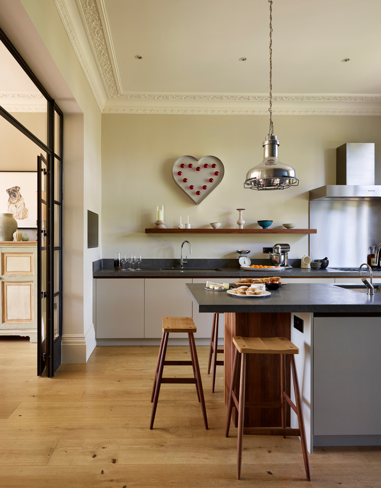 Inspiration for a large contemporary single-wall open plan kitchen in London with an integrated sink, flat-panel cabinets, white cabinets, limestone worktops, light hardwood flooring, an island, brown floors and black worktops.