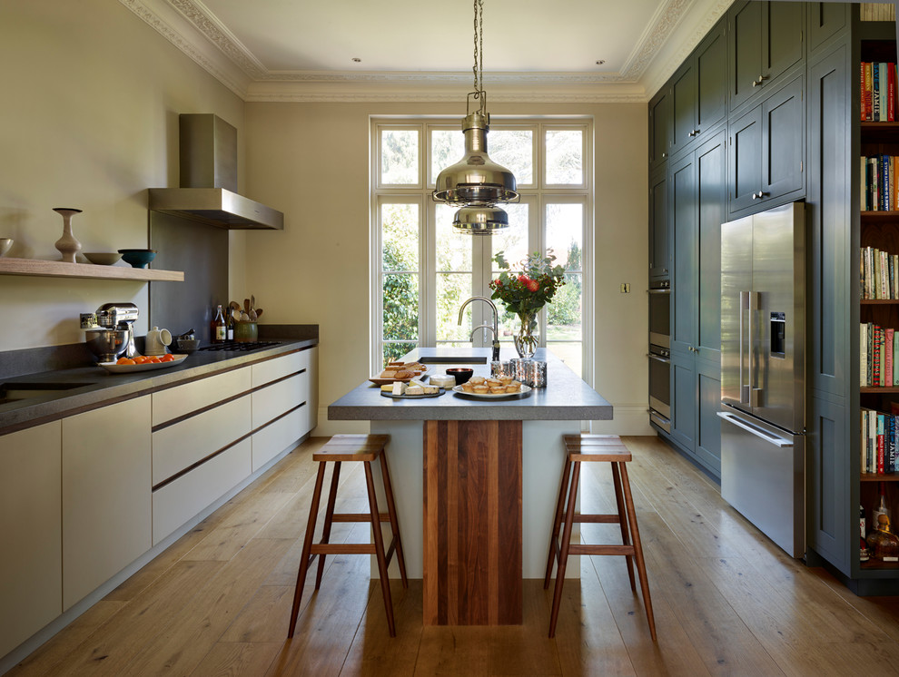 This is an example of a large contemporary galley kitchen in London with flat-panel cabinets, limestone worktops, an island, brown floors, black worktops, a submerged sink, beige cabinets, stainless steel appliances and medium hardwood flooring.