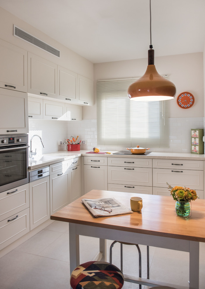 Photo of a classic l-shaped kitchen in Tel Aviv with white cabinets, white splashback, metro tiled splashback, stainless steel appliances and an island.