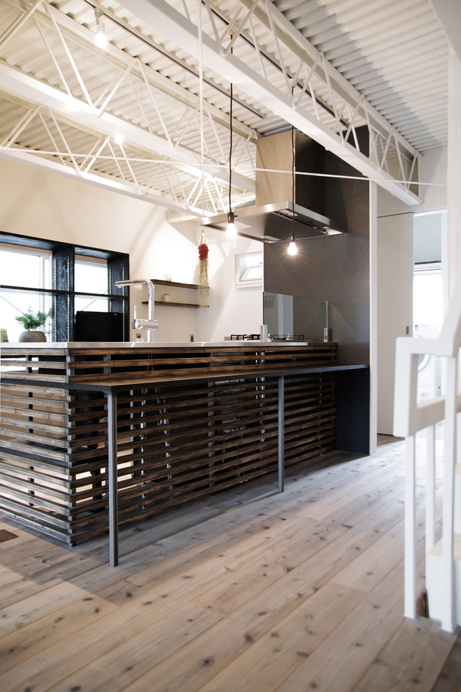 Foto på ett funkis linjärt kök och matrum, med bänkskiva i rostfritt stål, ljust trägolv och en halv köksö