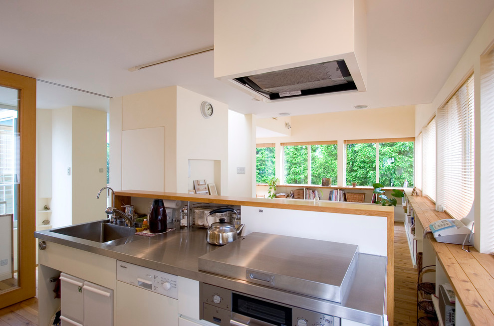 Moderne Küche mit integriertem Waschbecken, Edelstahl-Arbeitsplatte und braunem Holzboden in Tokio