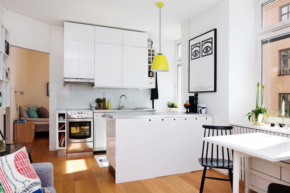 Источник вдохновения для домашнего уюта: параллельная кухня-гостиная среднего размера в скандинавском стиле с плоскими фасадами, белыми фасадами, техникой из нержавеющей стали, светлым паркетным полом, полуостровом и одинарной мойкой