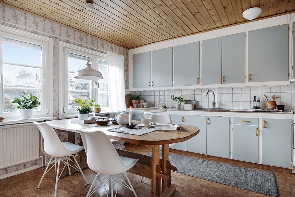 Bild på ett shabby chic-inspirerat kök och matrum, med en integrerad diskho, släta luckor, blå skåp, bänkskiva i rostfritt stål, vitt stänkskydd och brunt golv
