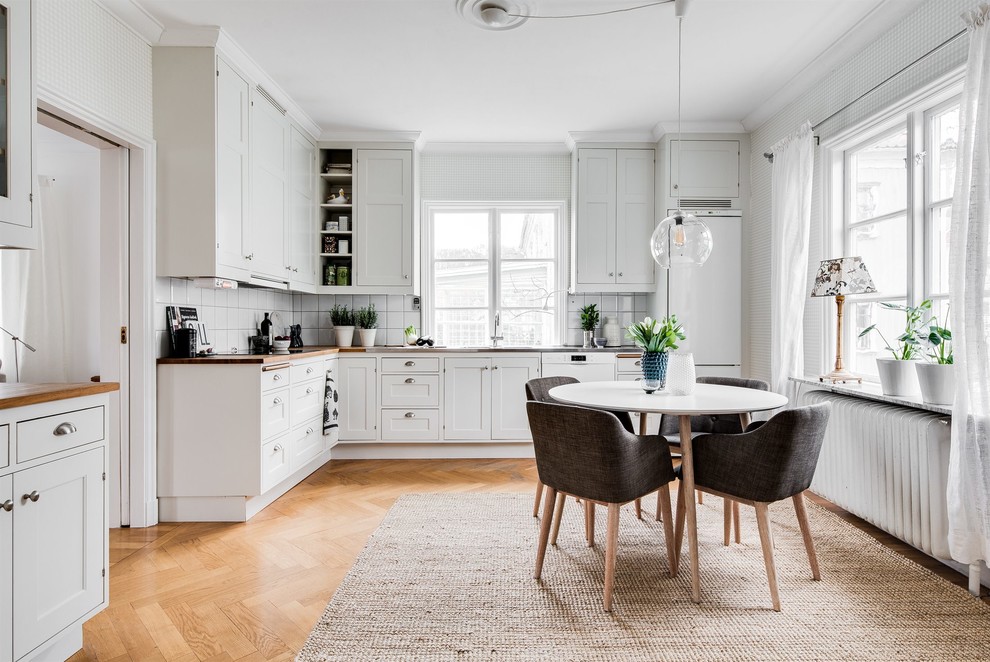Idéer för att renovera ett avskilt skandinaviskt l-kök, med luckor med infälld panel, vita skåp, träbänkskiva, vitt stänkskydd, vita vitvaror, ljust trägolv och beiget golv