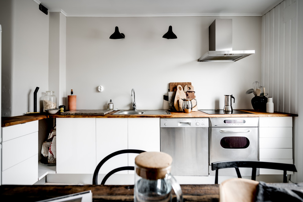 This is an example of a scandi l-shaped kitchen/diner in Gothenburg with a built-in sink, flat-panel cabinets, white cabinets, wood worktops, white splashback, stainless steel appliances and brown worktops.