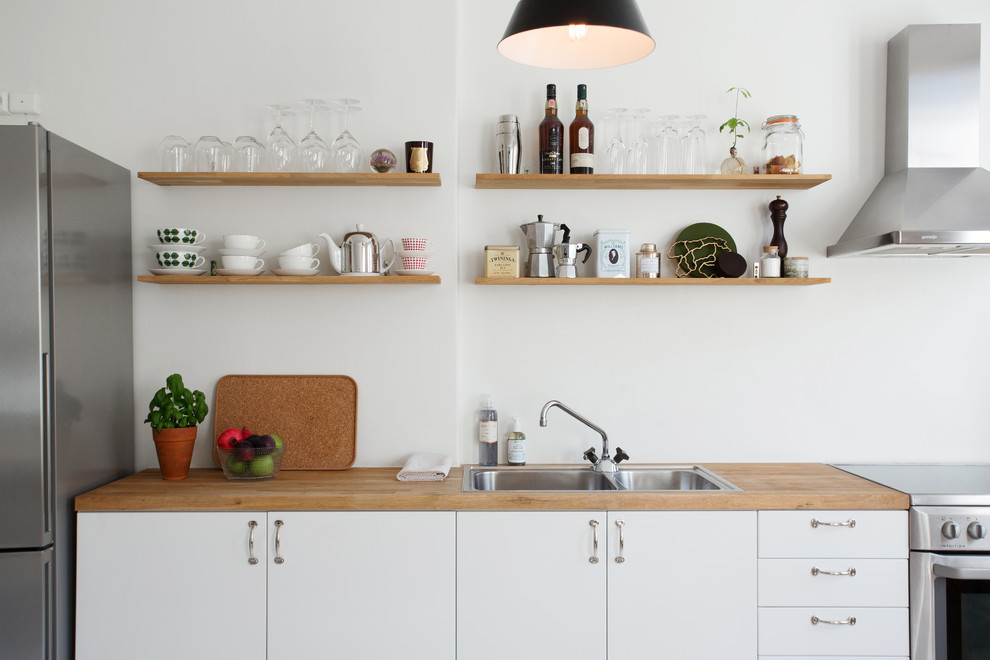 Foto på ett mellanstort skandinaviskt linjärt kök, med vita skåp, rostfria vitvaror, en dubbel diskho, släta luckor och träbänkskiva