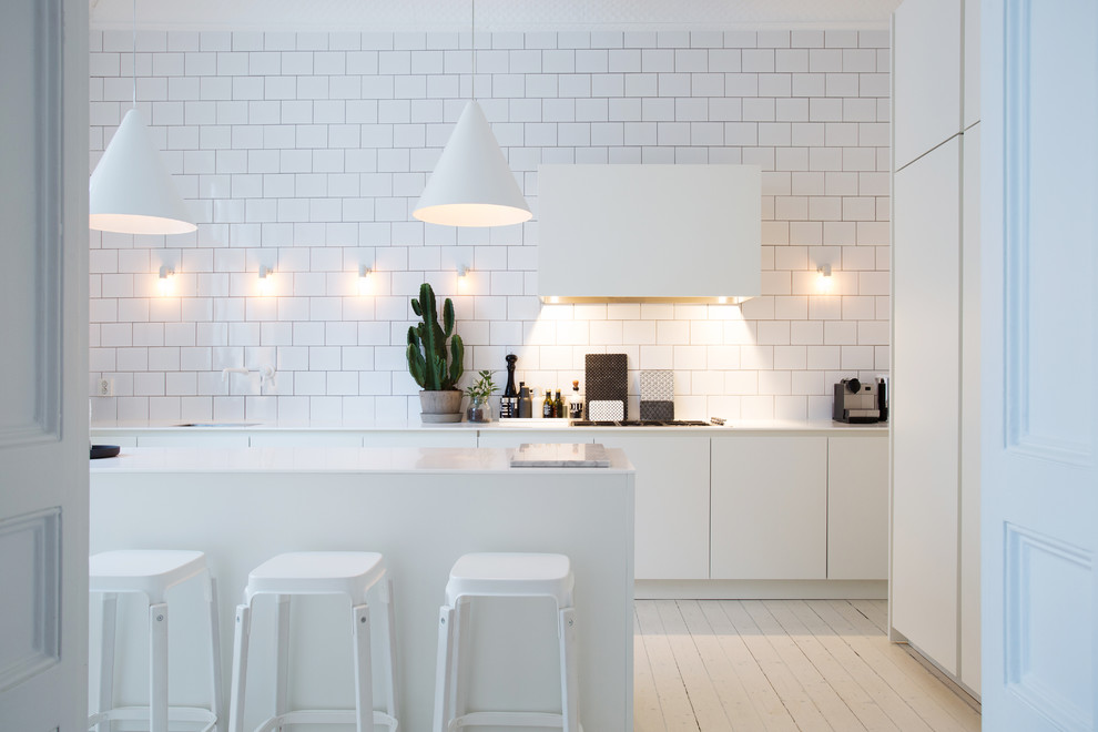 Einzeilige, Mittelgroße Nordische Wohnküche mit flächenbündigen Schrankfronten, weißen Schränken, Küchenrückwand in Weiß, Rückwand aus Metrofliesen, gebeiztem Holzboden, Kücheninsel, Marmor-Arbeitsplatte und weißen Elektrogeräten in Stockholm