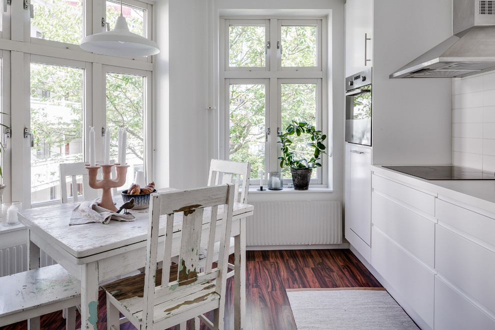Inredning av ett minimalistiskt mellanstort linjärt kök och matrum, med släta luckor, vita skåp, vitt stänkskydd, stänkskydd i tunnelbanekakel, mörkt trägolv och rostfria vitvaror