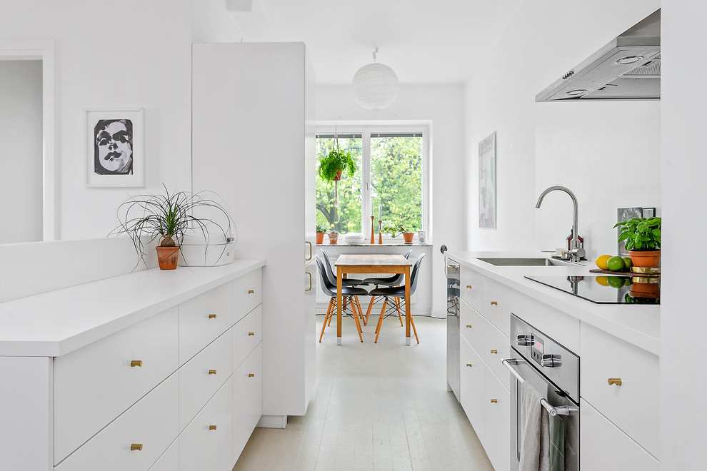 Foto på ett skandinaviskt kök, med en nedsänkt diskho, släta luckor, vita skåp, spegel som stänkskydd, rostfria vitvaror, en halv köksö och beiget golv