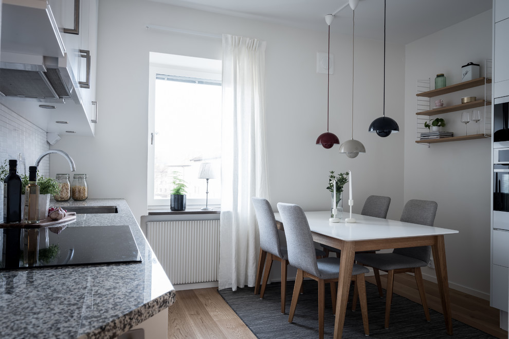 Idéer för skandinaviska grått kök, med en undermonterad diskho, släta luckor, vita skåp, vitt stänkskydd, stänkskydd i mosaik, svarta vitvaror, ljust trägolv och beiget golv