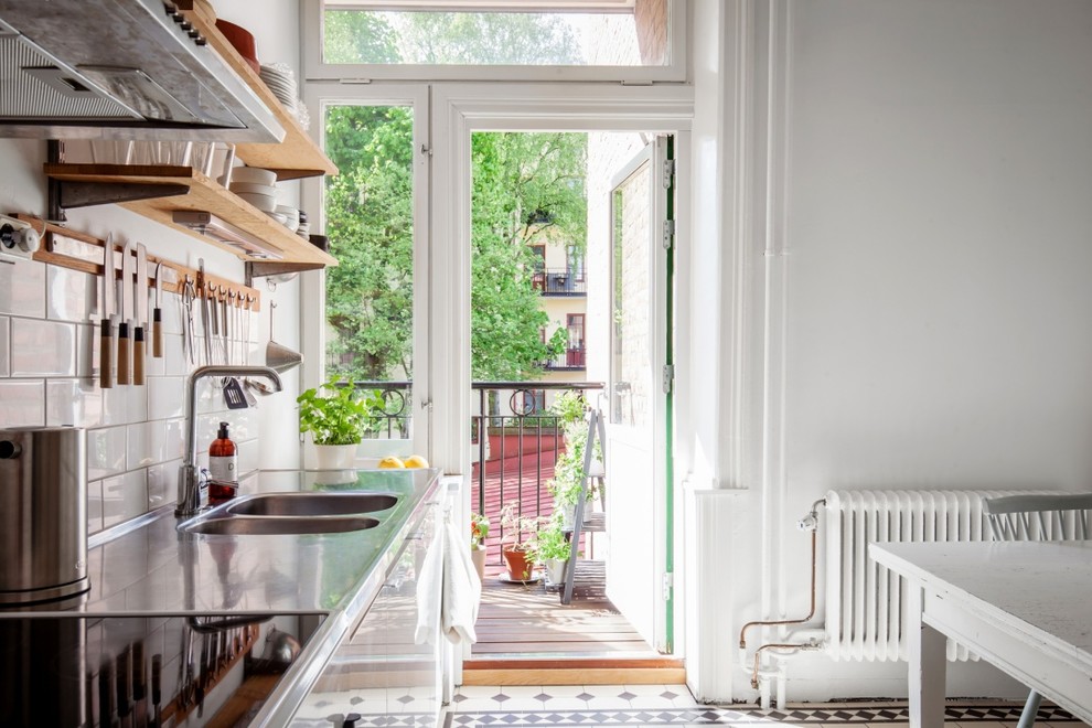 Foto på ett mellanstort skandinaviskt linjärt kök och matrum, med en dubbel diskho, bänkskiva i rostfritt stål, stänkskydd i tunnelbanekakel, klinkergolv i keramik, släta luckor, vita skåp och vitt stänkskydd