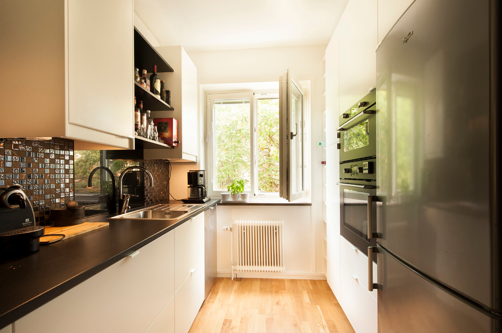 Geschlossene, Einzeilige Moderne Küche mit weißen Schränken, schwarzen Elektrogeräten und hellem Holzboden in Stockholm