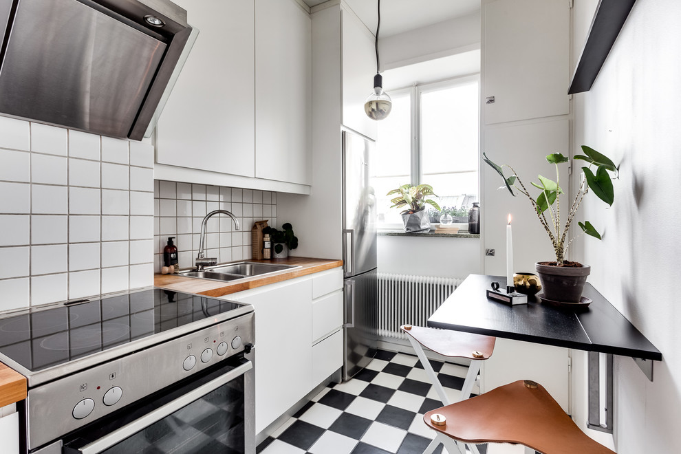 Bild på ett mellanstort skandinaviskt linjärt kök och matrum, med en dubbel diskho, släta luckor, vita skåp, träbänkskiva, vitt stänkskydd, rostfria vitvaror och klinkergolv i keramik