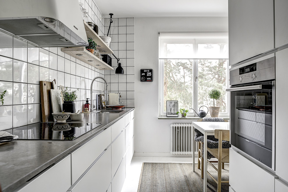 Bild på ett mellanstort skandinaviskt linjärt kök och matrum, med en undermonterad diskho, släta luckor, vita skåp, vitt stänkskydd och rostfria vitvaror