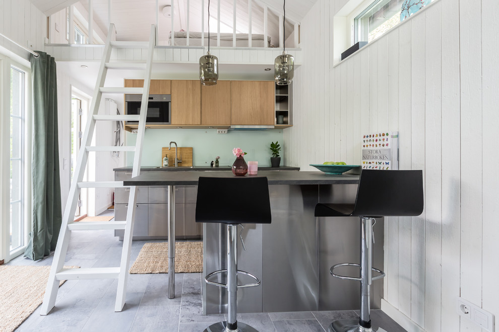 Cette image montre une cuisine ouverte nordique en inox avec un placard à porte plane, une crédence verte, un électroménager en acier inoxydable, une péninsule, un sol gris et plan de travail noir.