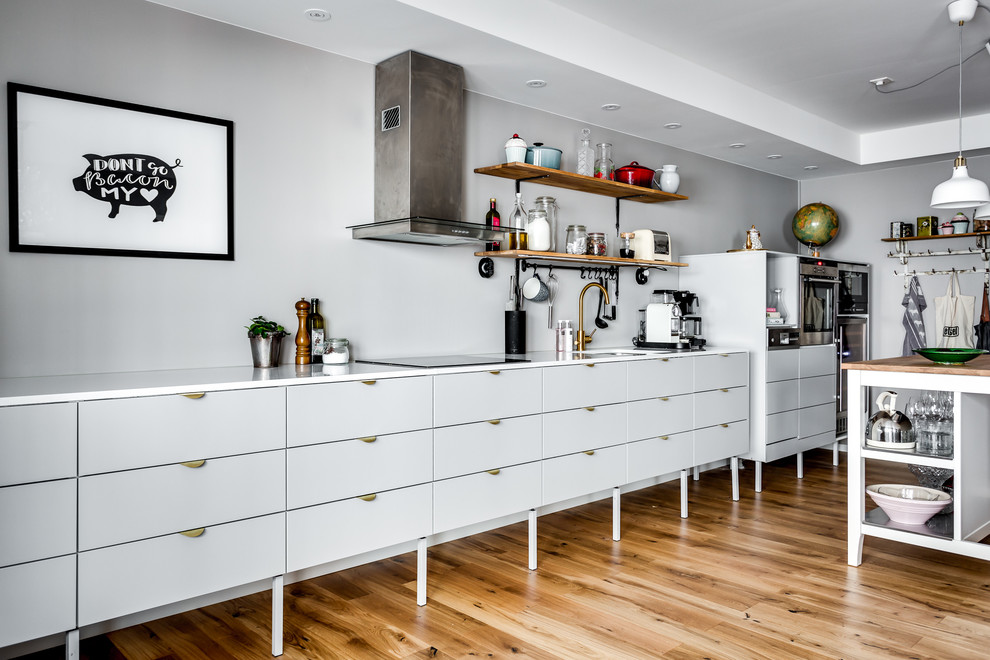 Medium sized industrial single-wall open plan kitchen in Stockholm with flat-panel cabinets, grey cabinets, grey splashback, stainless steel appliances, medium hardwood flooring and an island.