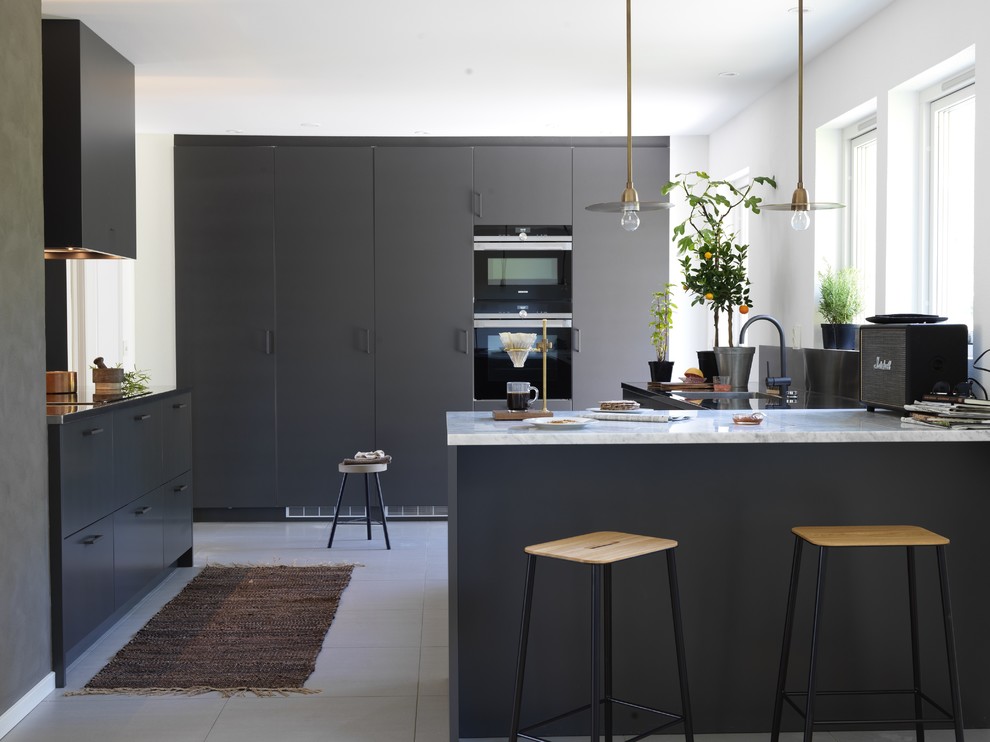 Свежая идея для дизайна: угловая кухня-гостиная среднего размера в скандинавском стиле с врезной мойкой, плоскими фасадами, серыми фасадами, мраморной столешницей, черным фартуком, черной техникой и островом - отличное фото интерьера