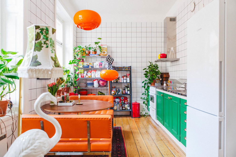 Einzeilige, Mittelgroße Eklektische Wohnküche ohne Insel mit profilierten Schrankfronten, grünen Schränken, Küchenrückwand in Weiß, weißen Elektrogeräten, braunem Holzboden und Edelstahl-Arbeitsplatte in Stockholm