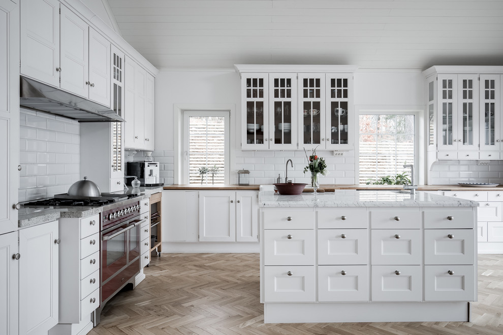 Inspiration for a country l-shaped medium tone wood floor and beige floor open concept kitchen remodel in Gothenburg with recessed-panel cabinets, white cabinets, marble countertops, white backsplash, black appliances, an island and subway tile backsplash