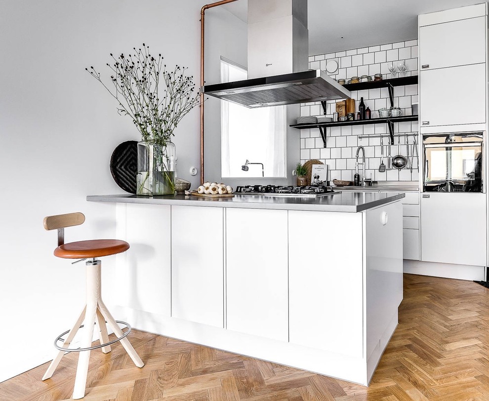 Foto på ett litet minimalistiskt kök, med en undermonterad diskho, släta luckor, vita skåp, vitt stänkskydd, svarta vitvaror, ljust trägolv, en halv köksö och beiget golv
