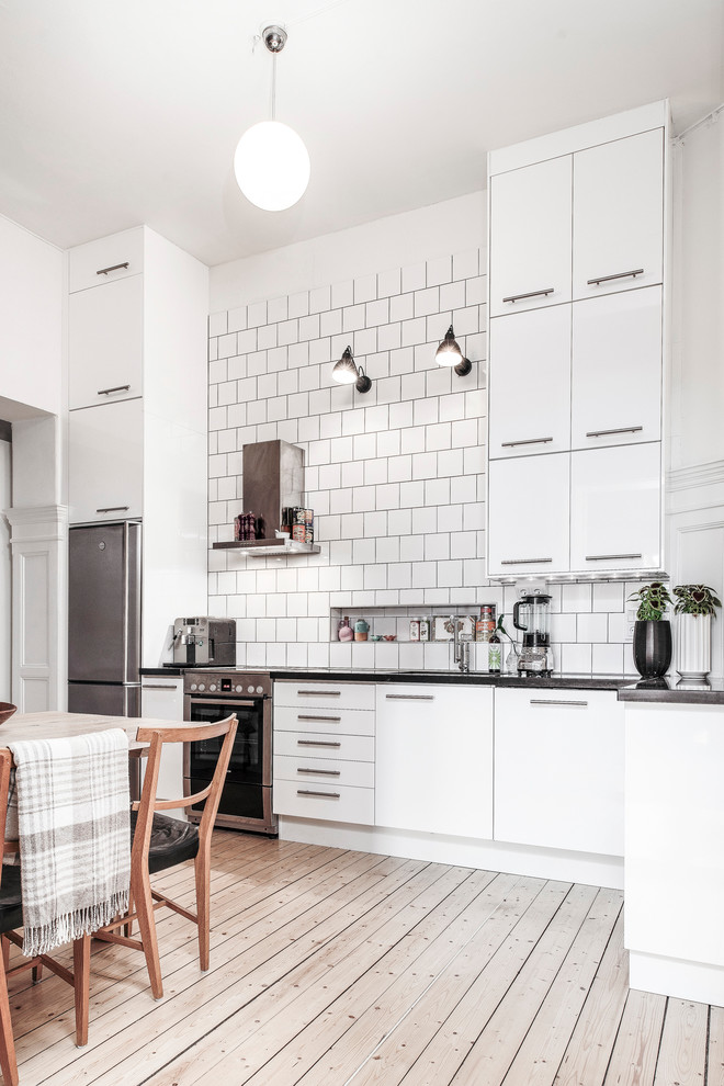 Mid-sized danish l-shaped light wood floor eat-in kitchen photo in Gothenburg with flat-panel cabinets, white cabinets, white backsplash and stainless steel appliances