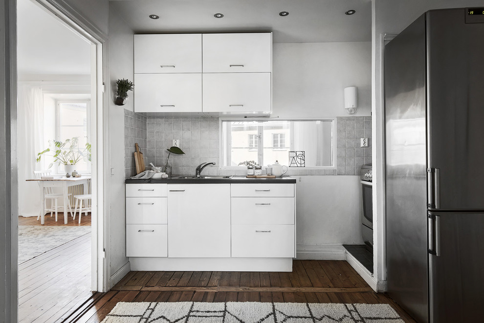 Immagine di una cucina nordica chiusa con ante lisce, ante bianche, elettrodomestici in acciaio inossidabile, parquet scuro e nessuna isola
