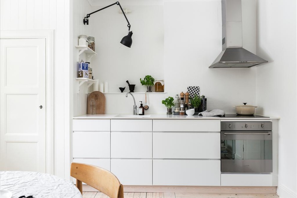This is an example of a medium sized scandi single-wall kitchen/diner in Gothenburg with flat-panel cabinets, white cabinets, stainless steel appliances, light hardwood flooring, no island and white splashback.