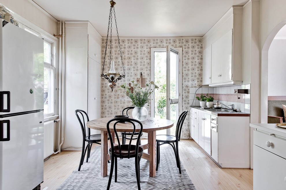 Immagine di una cucina parallela nordica con ante lisce, ante bianche, paraspruzzi bianco, elettrodomestici bianchi, parquet chiaro, pavimento beige e top marrone