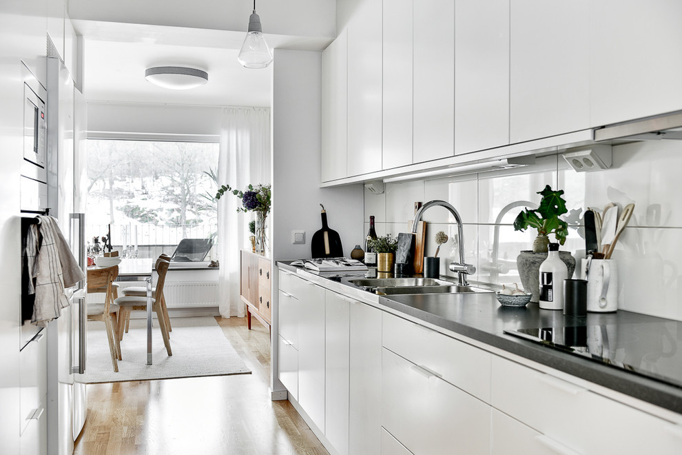 Inspiration for a medium sized scandinavian galley enclosed kitchen in Stockholm with a built-in sink, flat-panel cabinets, white cabinets, white splashback and medium hardwood flooring.
