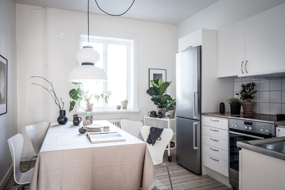 Inspiration for a small scandi l-shaped kitchen/diner in Gothenburg with flat-panel cabinets, white cabinets, white splashback, porcelain splashback, stainless steel appliances, light hardwood flooring and beige floors.