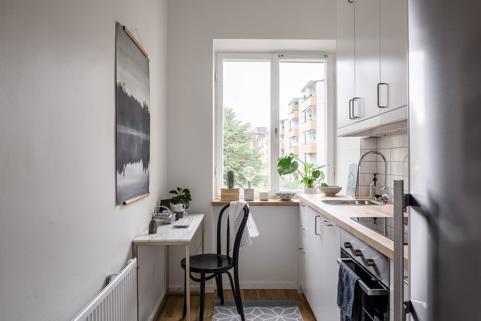 Einzeilige, Kleine Skandinavische Wohnküche ohne Insel mit flächenbündigen Schrankfronten, weißen Schränken, Arbeitsplatte aus Holz, Küchenrückwand in Weiß, braunem Holzboden und braunem Boden in Stockholm