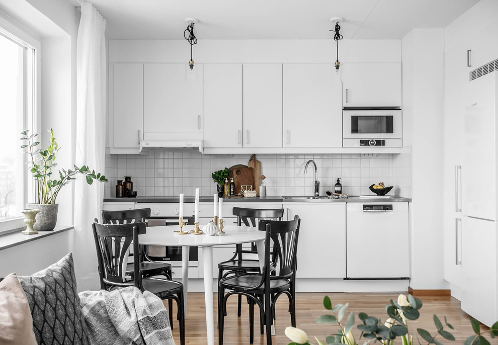 Exempel på ett skandinaviskt grå linjärt grått kök med öppen planlösning, med släta luckor, vita skåp, bänkskiva i rostfritt stål, vitt stänkskydd, beiget golv, vita vitvaror och ljust trägolv