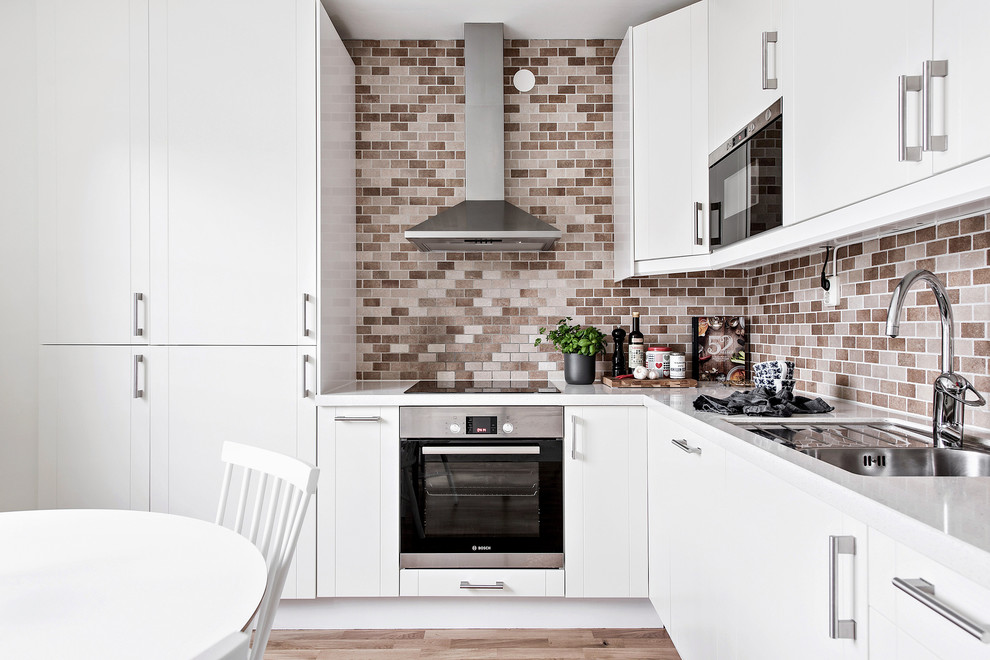 Exempel på ett nordiskt kök, med en dubbel diskho, släta luckor, vita skåp, brunt stänkskydd, stänkskydd i tunnelbanekakel, svarta vitvaror, ljust trägolv och brunt golv
