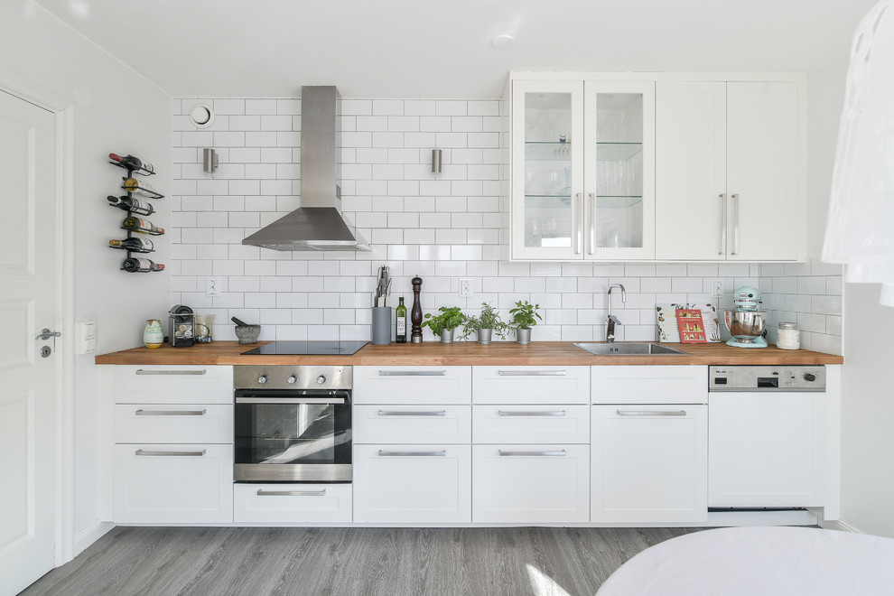 Minimalistisk inredning av ett linjärt kök och matrum, med en enkel diskho, skåp i shakerstil, vita skåp, träbänkskiva, vitt stänkskydd, stänkskydd i tunnelbanekakel och rostfria vitvaror