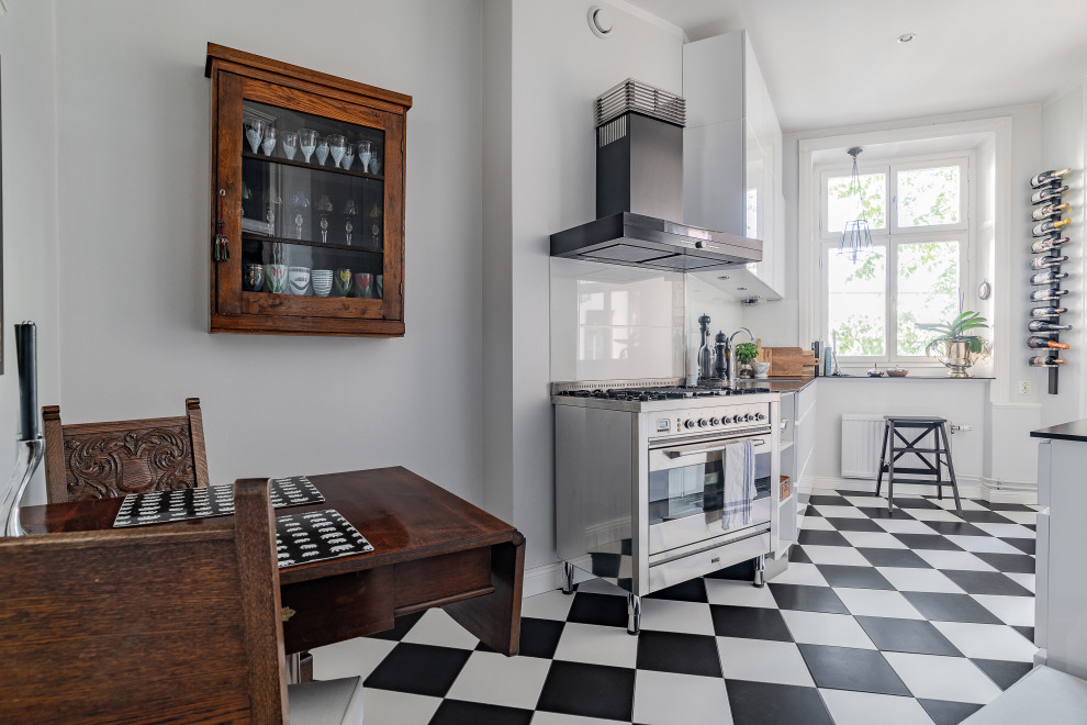 ストックホルムにある北欧スタイルのおしゃれなダイニングキッチン (フラットパネル扉のキャビネット、白いキャビネット、ガラスタイルのキッチンパネル、シルバーの調理設備、アイランドなし、マルチカラーの床、黒いキッチンカウンター) の写真